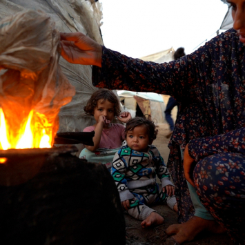 Sem acesso a gás de cozinha, Yasmin, deslocada pela guerra em Gaza, precisa acender uma fogueira usando plástico para preparar uma refeição para os seus filhos. © Ibrahim Nofal