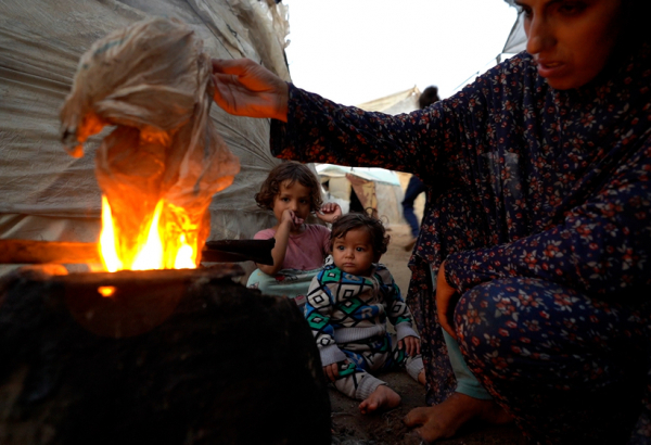 Sem acesso a gás de cozinha, Yasmin, deslocada pela guerra em Gaza, precisa acender uma fogueira usando plástico para preparar uma refeição para os seus filhos. © Ibrahim Nofal